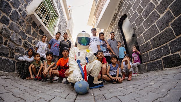 pexels-photo-27952870-27952870 Group of kids and an astronaut playing with a soccer ball in a narrow urban street.